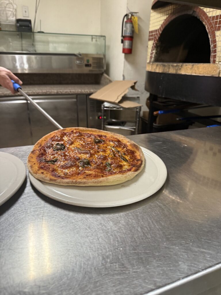 Freshly baked Neapolitan-style pizza on a plate in a commercial kitchen with a wood-fired oven in the background