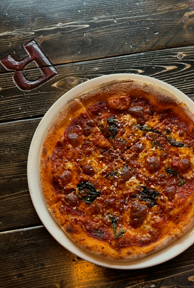 Wood-fired Neapolitan pizza with tomato sauce, melted cheese, and basil served on a plate on a rustic wooden table