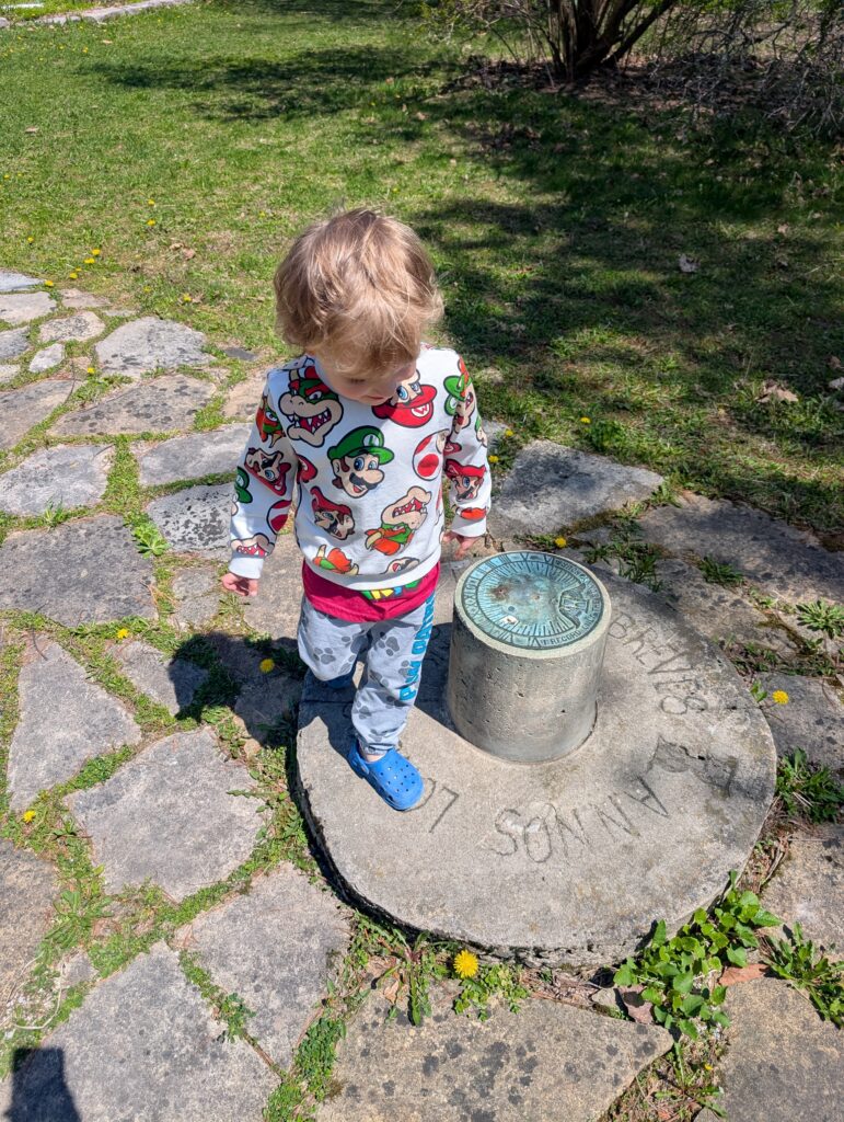 Child standing beside a stone garden marker on a path, exploring outdoor features at the Leacock Museum
