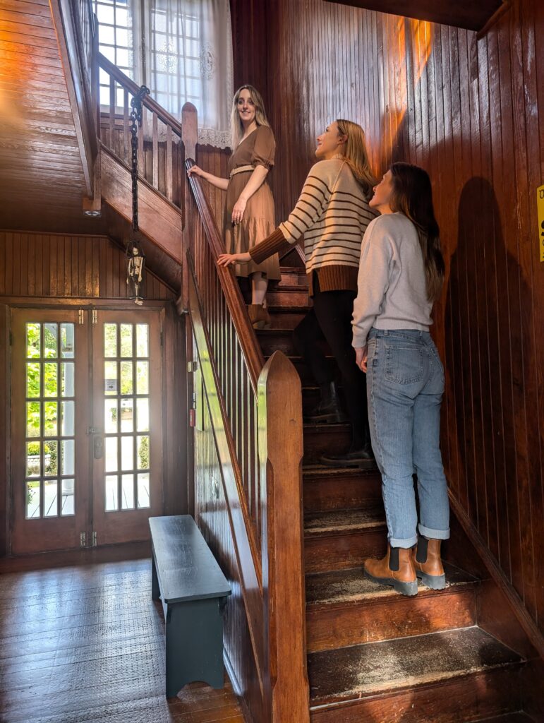 Three adults walking up a wooden staircase inside a historic home with warm wood paneling and natural light