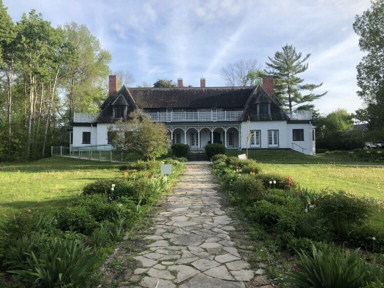 Stone pathway leading through garden beds toward the historic Leacock house surrounded by green lawn and trees